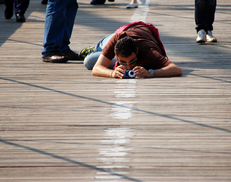 Photo: a man with a camera lies on the wooden planks of a bridge to take pictures