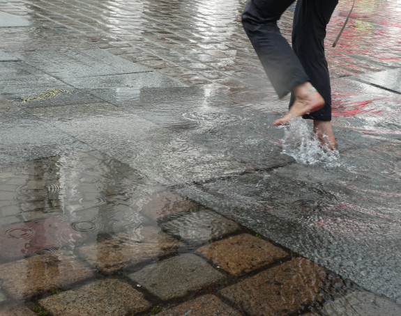 Photo: a person jumps barefoot over a square flooded by rainwater