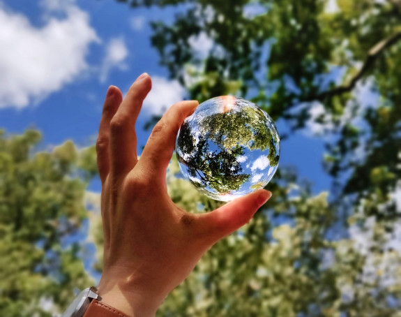 Glaskugel wird in der Hand gehalten, Baumkronen und Himmeln spiegeln sich darin 