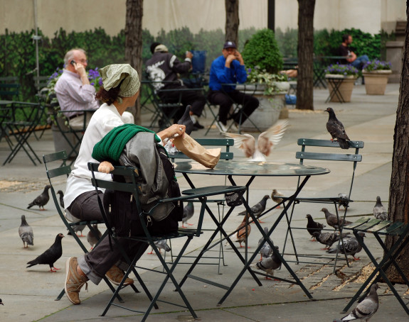Foto: eine Frau sitzt an einem Tisch im Park und füttert Tauben