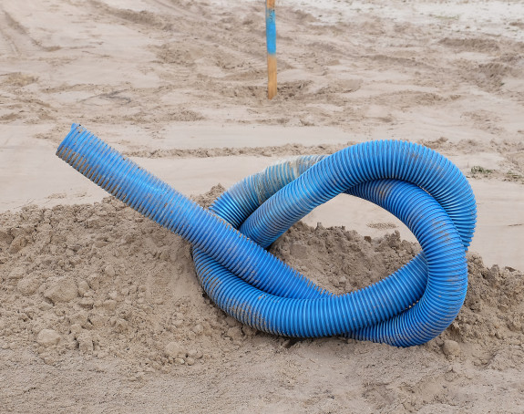Foto: ein blaues Plastikrohr liegt verknotet im Sand
