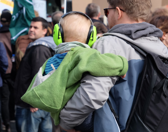 Foto: Vater hält ein Kleinkind mit Kopfhörern auf dem Arm